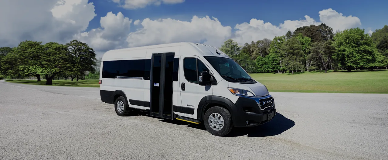 white passenger van parked on a gravel lot with grass and tree-line in the background
