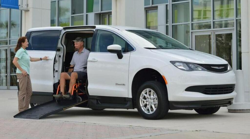 Two people using a wheelchair ramp on an accessible van.