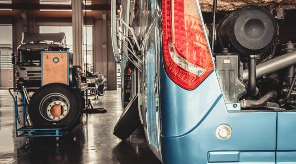 A blue bus is undergoing maintenance in a garage.