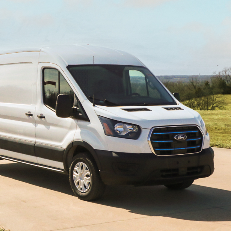 A white ford cargo transit van is parked in front of a grassy field.