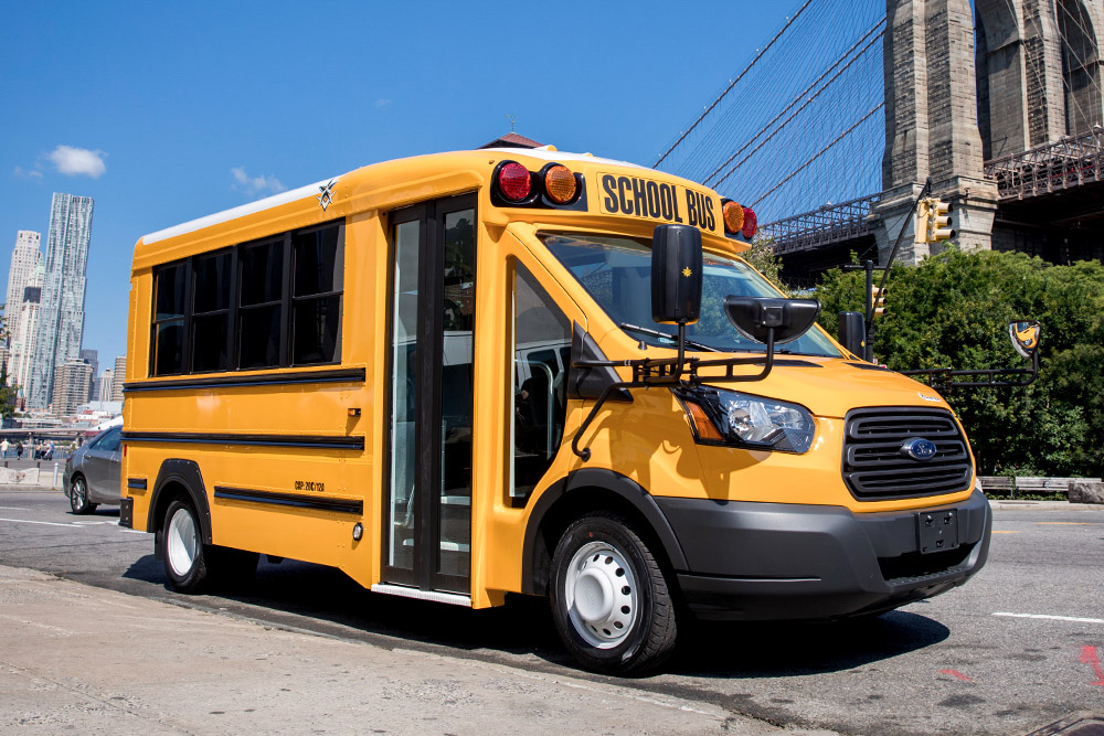 A yellow Trans Tech Trans Star school bus parked in front of the brooklyn bridge.