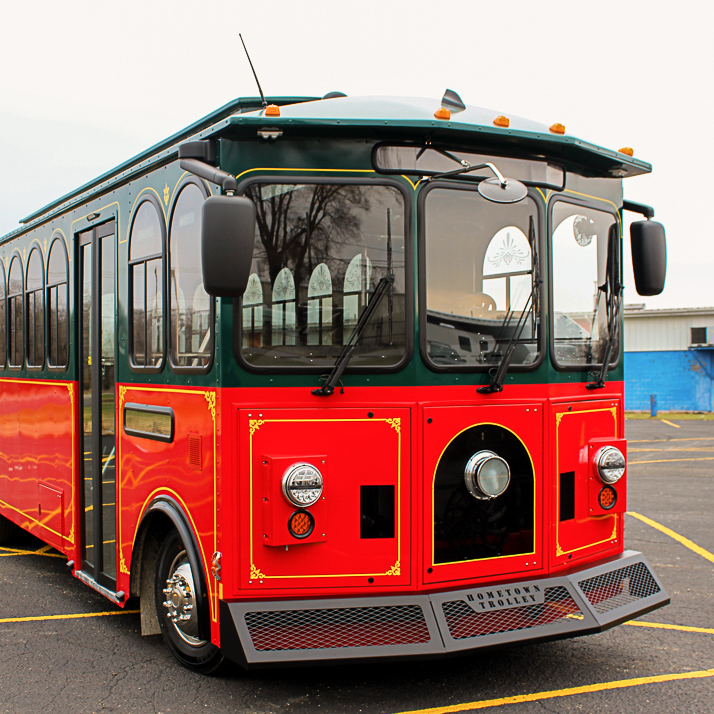 A red and green trolley bus parked in a parking lot.