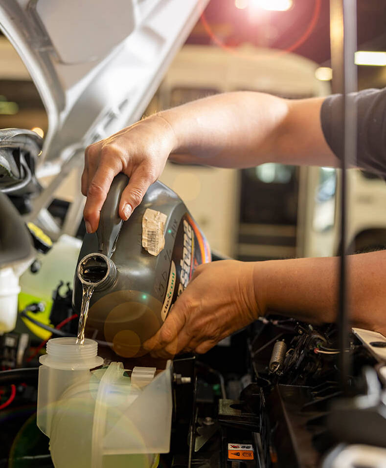 A man performing car maintenance by pouring coolant into the vehicle.