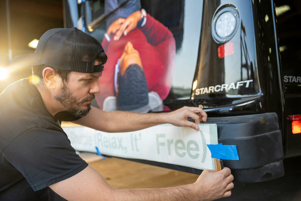 A man is putting tape on the back of a bus.