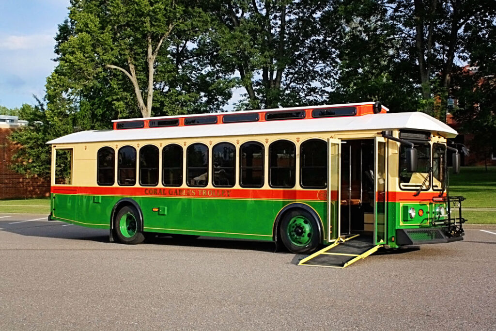 A green and tan Hometown Trolley Streetcar parked in a parking lot with a wheelchair ramp extended.
