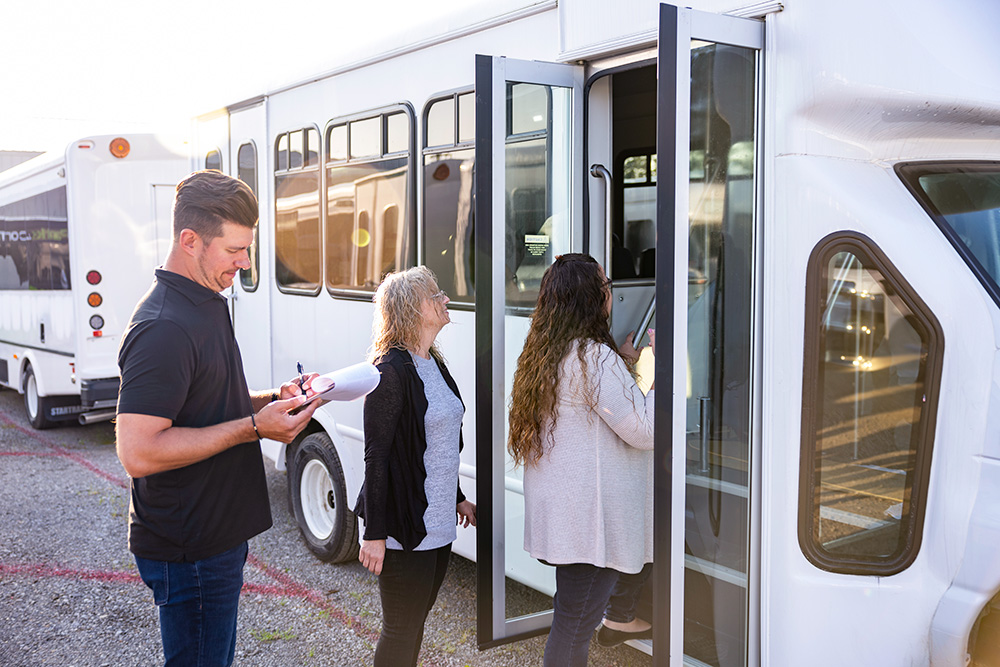 A group of people standing in front of a bus available for long-term rentals.