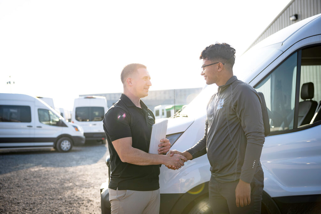 Two men shaking hands in front of a van.