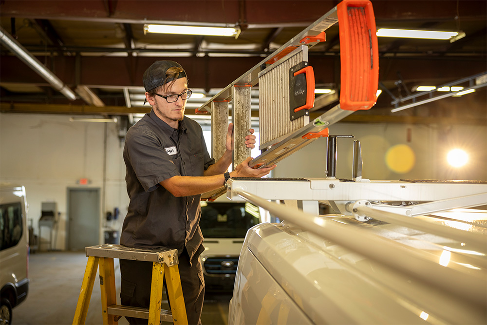 A man working on a ladder on top of a cargo van.