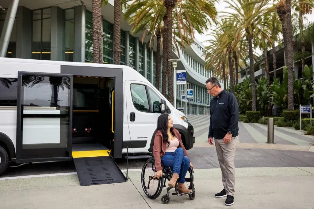 Person in wheelchair by low-floor vehicle.