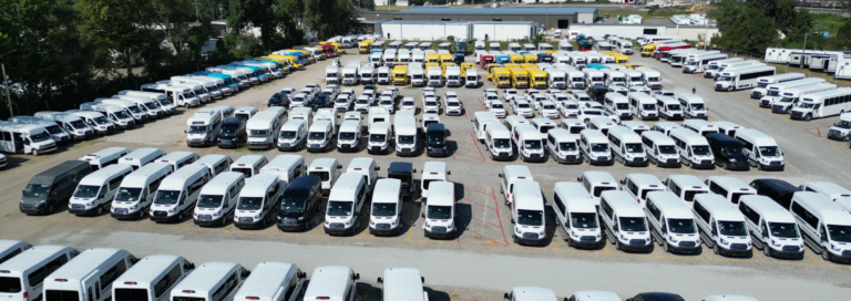 large fleet of commercial vans and school buses lined up on a dealership lot ready for deployment