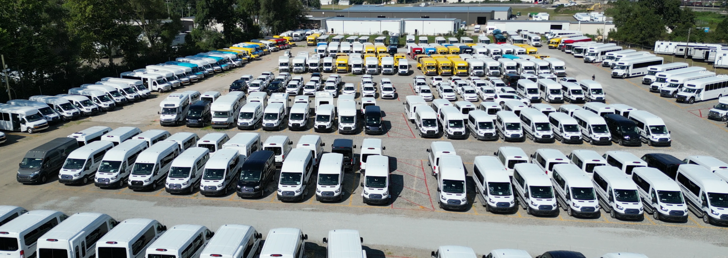large fleet of commercial vans and school buses lined up on a dealership lot ready for deployment
