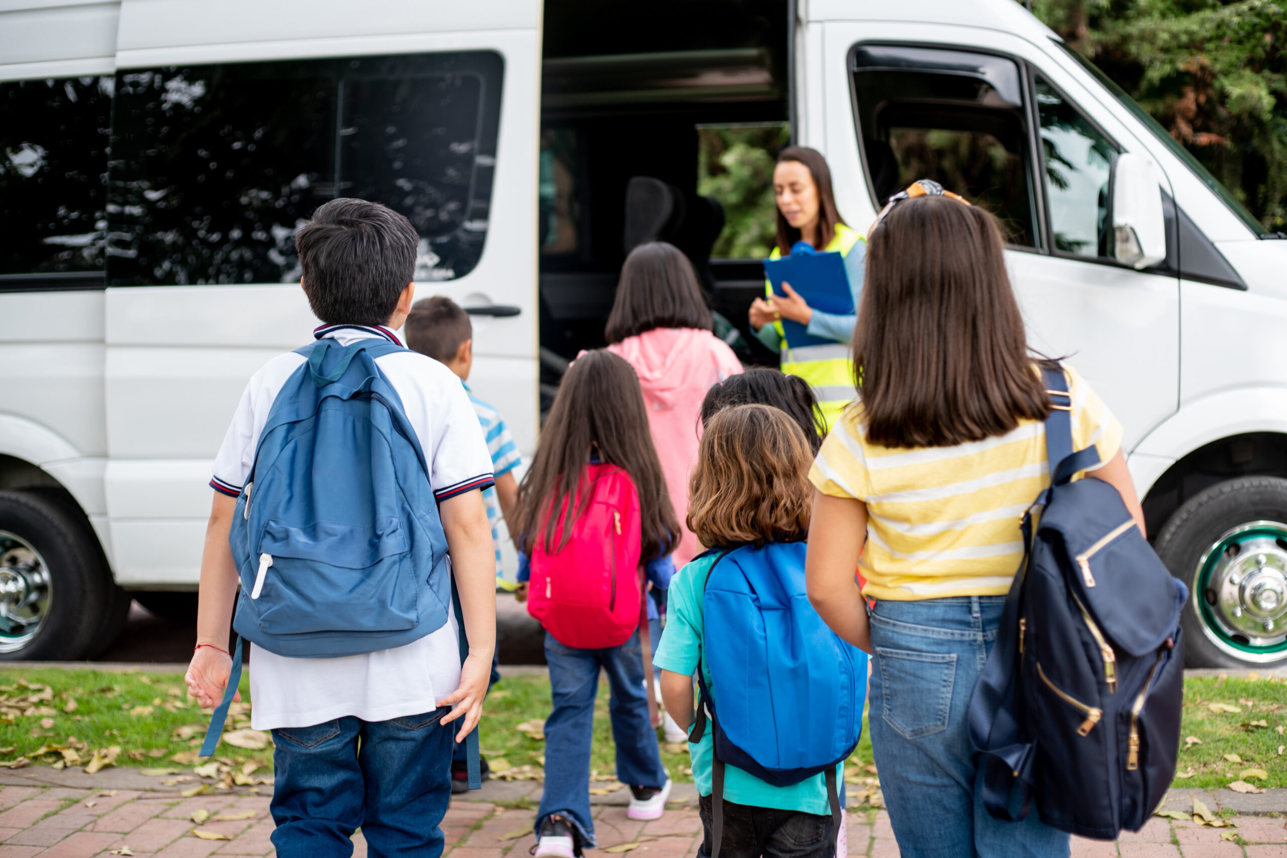 students boarding a school transportation passenger van with driver assistance during pickup