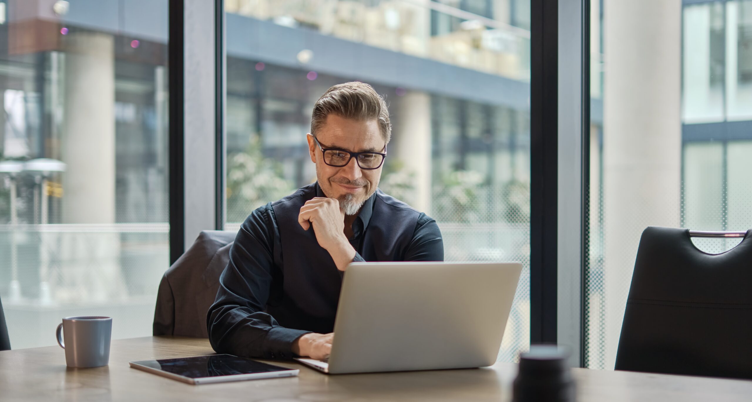 Business portrait - businessman using laptop computer in office, thinking. Happy middle aged man, entrepreneur working online.