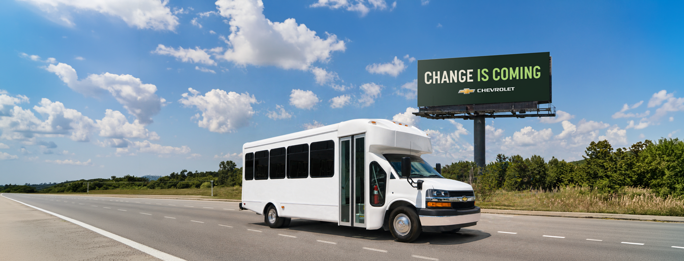 Chevrolet bus driving on a road past a billboard that says "change is coming."